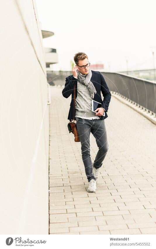 Young businessman walking in the street, carrying digital tablet and ear phones on the phone call telephoning On The Telephone calling Businessman Business man