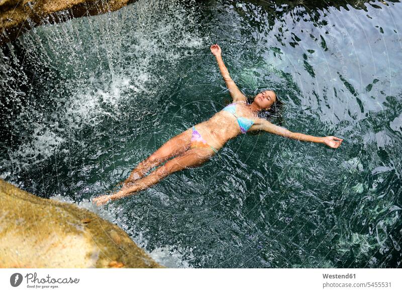 Young woman floating in water in pool with waterfall females women Adults grown-ups grownups adult people persons human being humans human beings vacation