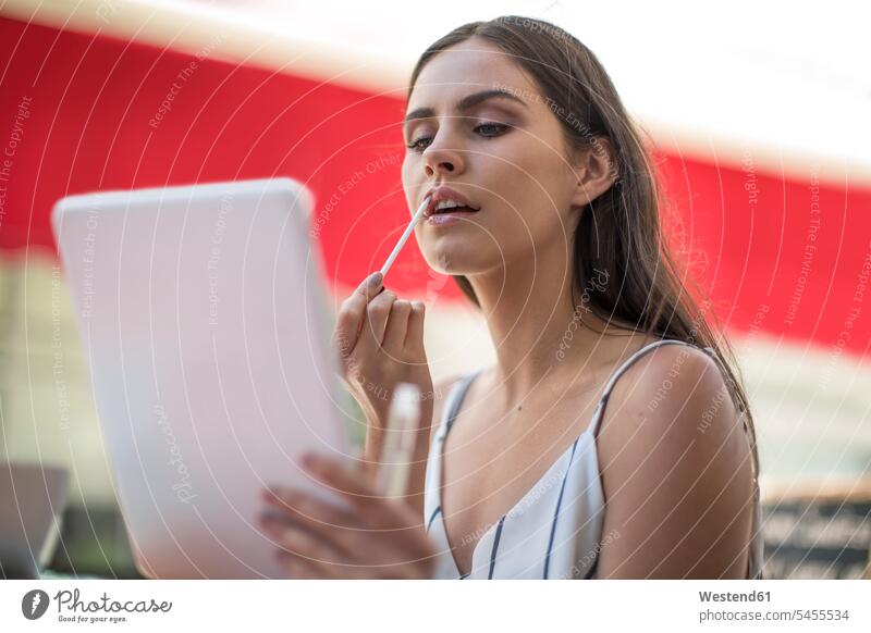 Young woman applying lip gloss holding digital tablet females women Adults grown-ups grownups adult people persons human being humans human beings caucasian