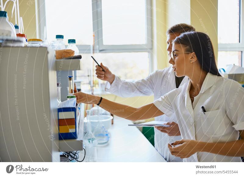 Young man and woman working together in laboratory At Work men males females women Adults grown-ups grownups adult people persons human being humans