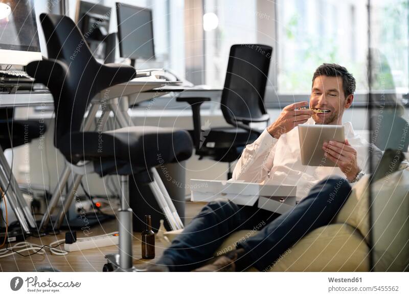 Businessman in bean bag in office eating pizza and using tablet Pizza Pizzas Business man Businessmen Business men digitizer Tablet Computer Tablet PC