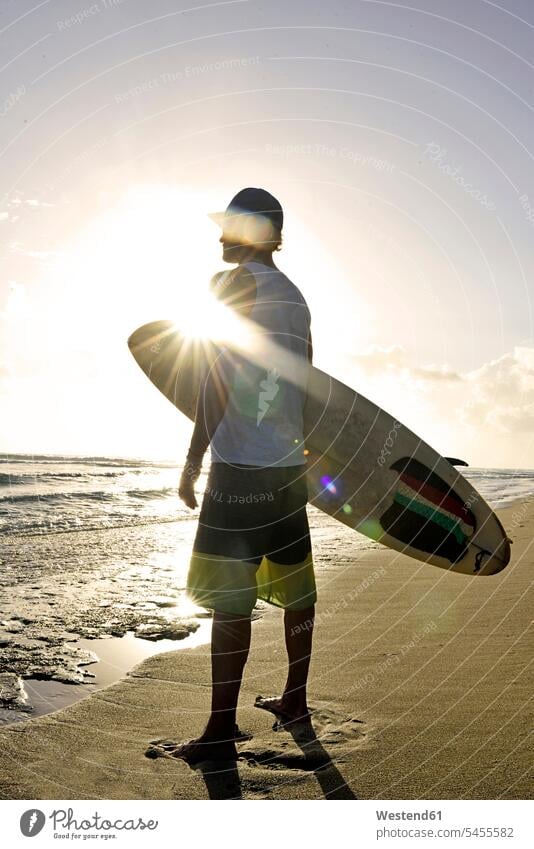 Man with surfboard standing on the beach watching sunset beaches man men males Adults grown-ups grownups adult people persons human being humans human beings