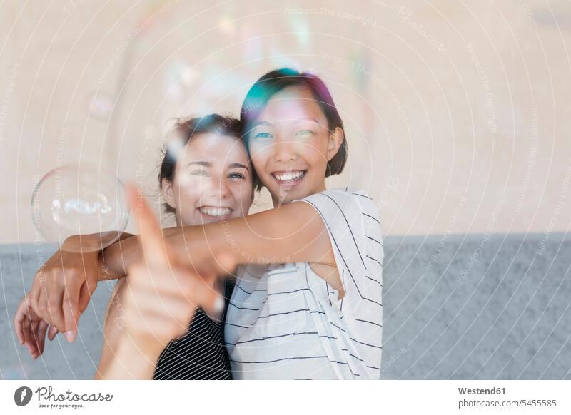 Two young women playing with soap bubbles female friends mate friendship watching looking looking at best friend bff best friends view seeing viewing caucasian