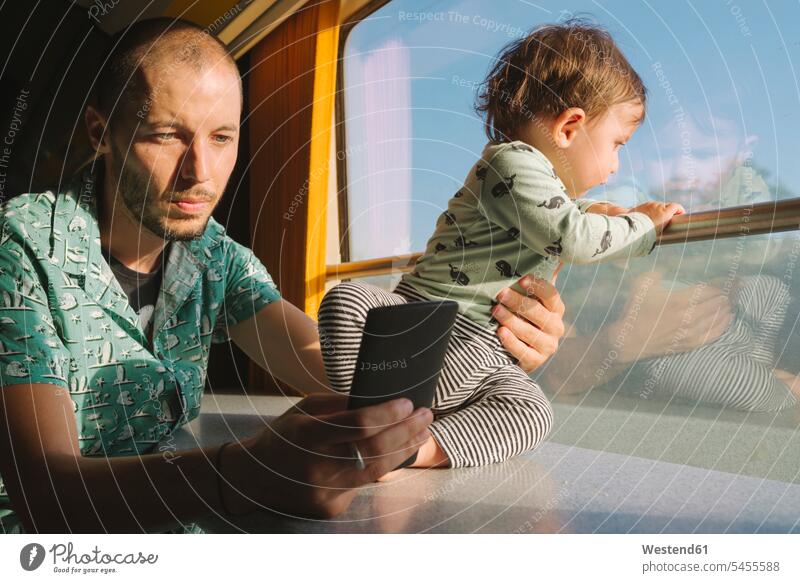Father holding his baby girl and using smartphone while traveling by train father pa fathers daddy dads papa travelling mobile phone mobiles mobile phones