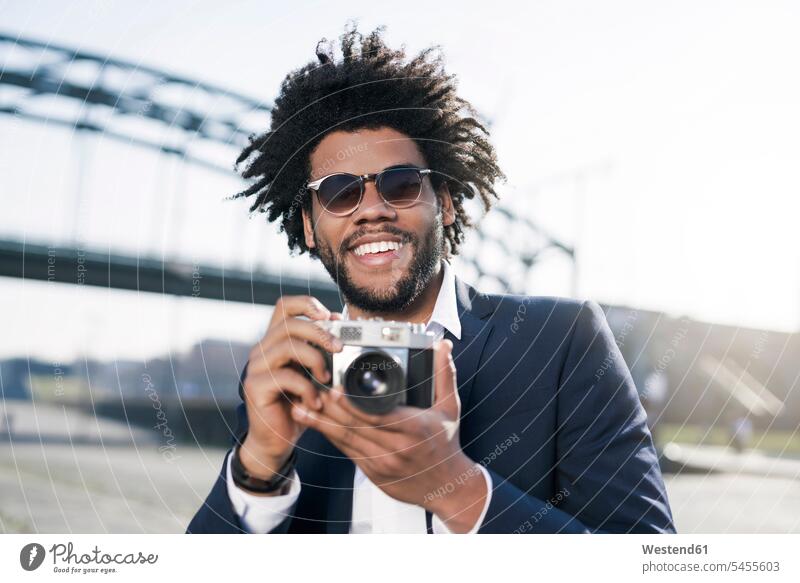 Smiling man in suit at the riverside holding a vintage camera men males cameras smiling smile Adults grown-ups grownups adult people persons human being humans