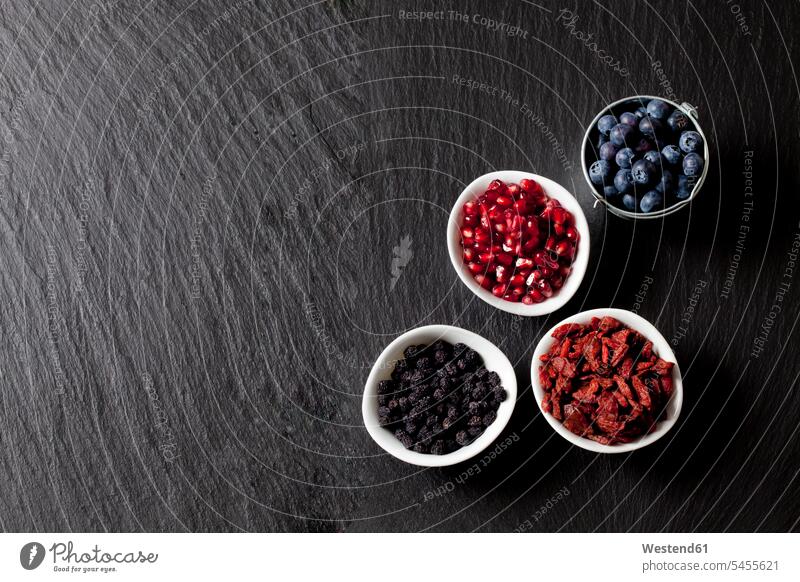 Bowls of blueberries, pomegranate seed, goji berries and chokeberries on slate food and drink Nutrition Alimentation Food and Drinks arrangement grouping
