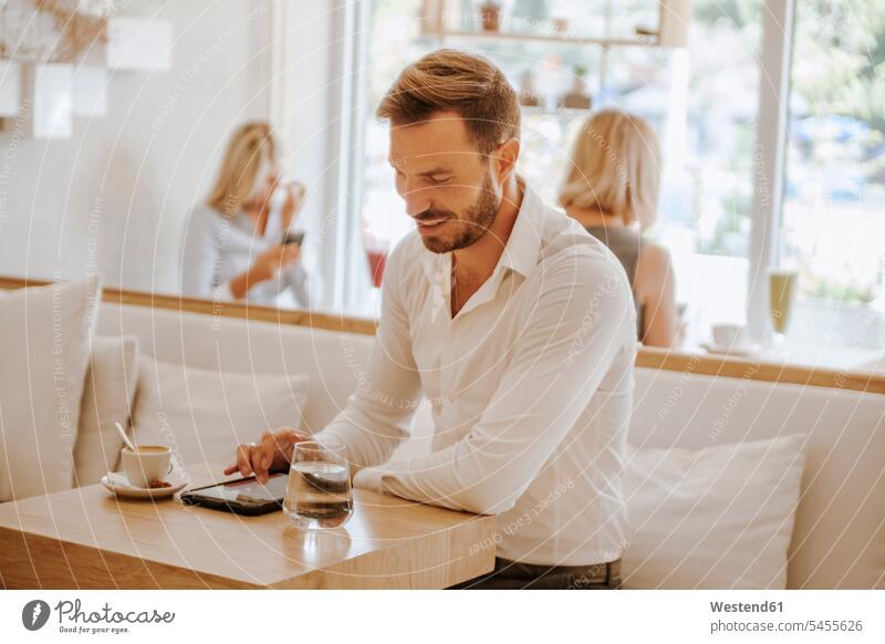 Man using tablet in a cafe with two women in background Businessman Business man Businessmen Business men males digitizer Tablet Computer Tablet PC