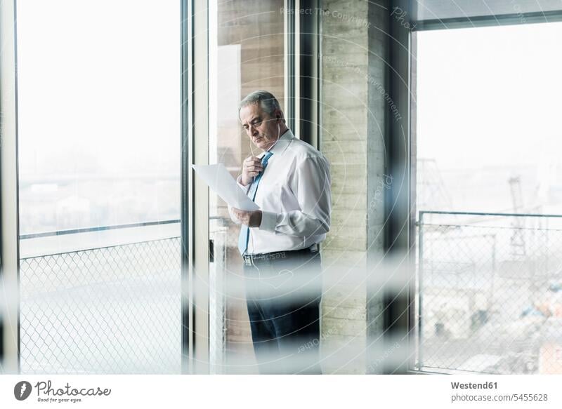 Senior manager in office standing at window talking on smartphone, holding document offices office room office rooms managers on the phone call telephoning