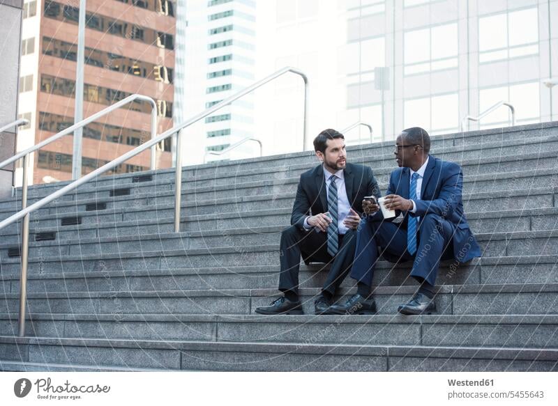 Two businessmen sitting on stairs talking colleagues stairway Businessman Business man Businessmen Business men speaking business people businesspeople