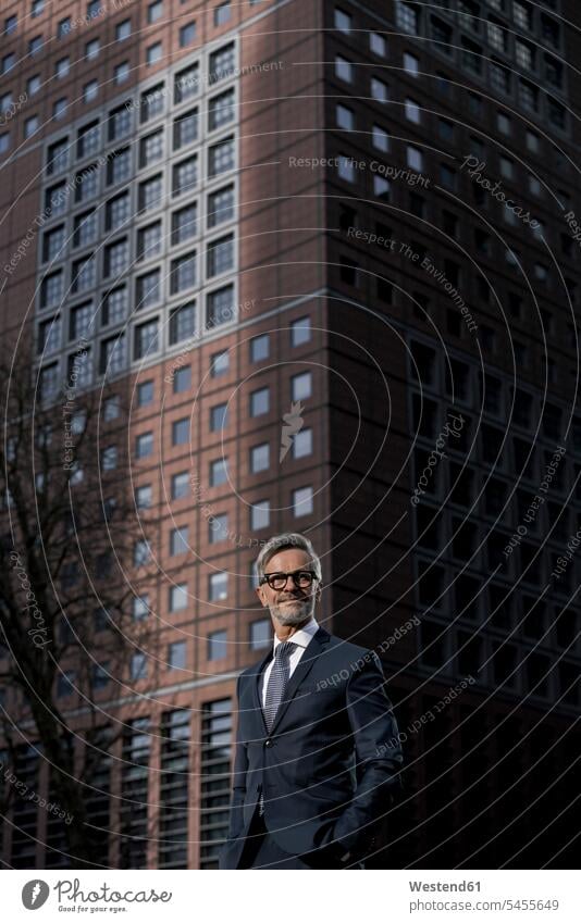 Grey-haired businessman in front of red skyscraper smiling smile Businessman Business man Businessmen Business men skyscrapers multistory building high rise