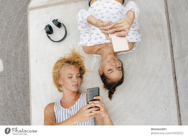 Two young women with cell phones lying on ramp in a skatepark female friends mobile phone mobiles mobile phones Cellphone laying down lie lying down Ramp woman