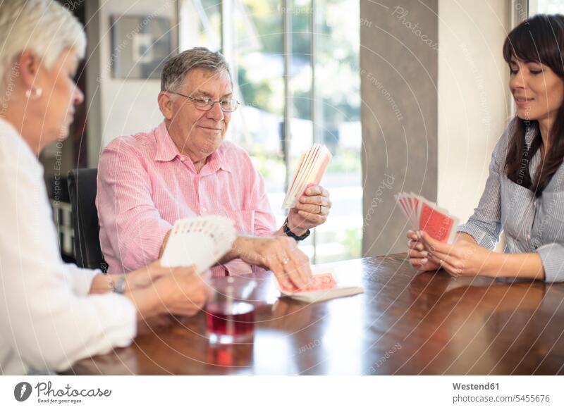 Senior couple playing cards with daughter at home daughters senior men senior man elder man elder men senior citizen twosomes partnership couples family