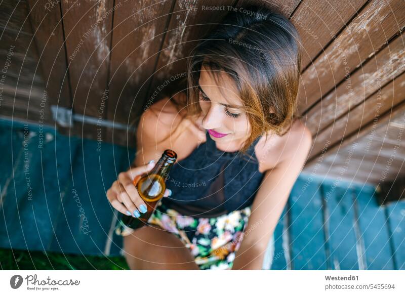 Young woman with beer sitting at wooden hut relaxed relaxation females women Beer Beers Ale Seated drinking relaxing Adults grown-ups grownups adult people