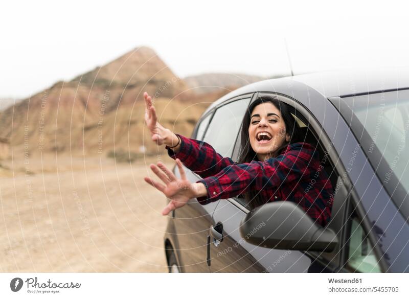 Spain, Navarra, Bardenas Reales, screaming and waving young woman leaning out of car window females women automobile Auto cars motorcars Automobiles Adults