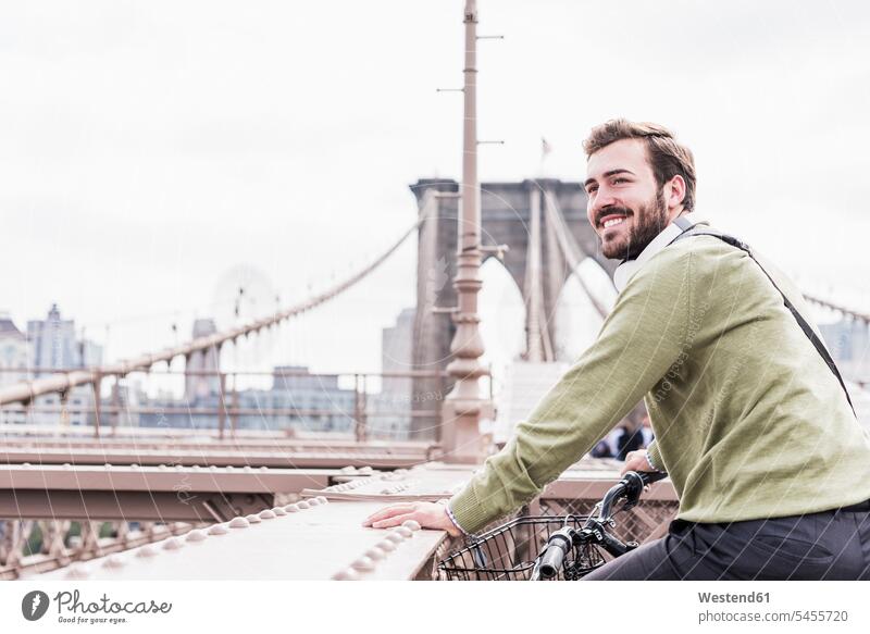 USA, New York City, smiling man on bicycle on Brooklyn Bridge smile bridge bridges bikes bicycles New York State men males transportation United States