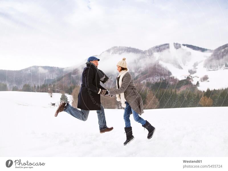 Happy senior couple jumping in the air in snow-covered landscape elder couples senior couples jump in the air Leaping adult couple adult couples twosomes