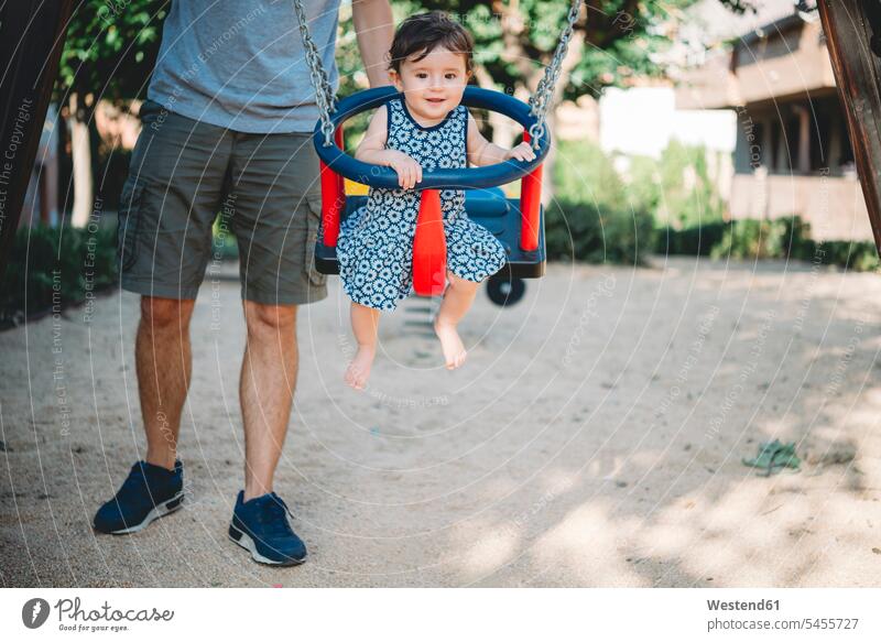 Father swinging his baby girl sitting in swing on playground swing set swingset baby girls female babies infants people persons human being humans human beings