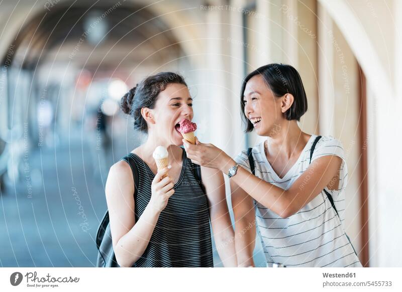 Two young women with ice cream cones female friends mate friendship multicultural summer summer time summery summertime tasting eating best friend bff