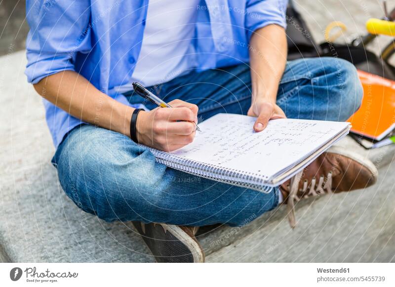 Young man sitting on bench writing on notepad, partial view write student students learning education benches men males hand human hand hands human hands Seated