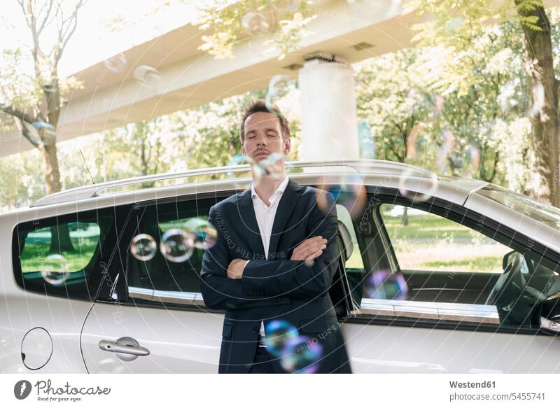 Businessman standing next to car surrounded by soap bubbles Business man Businessmen Business men business people businesspeople business world business life