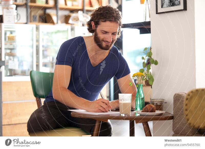 Smiling young man sitting in a coffee shop writing letter write men males cafe Adults grown-ups grownups adult people persons human being humans human beings
