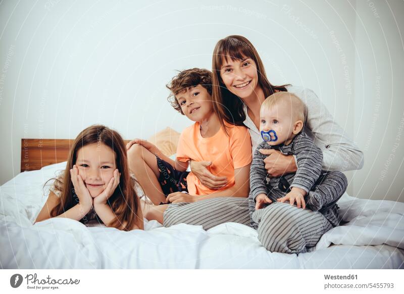 Happy mother in bed with her three children portrait portraits mommy mothers ma mummy mama beds smiling smile family families parents people persons human being