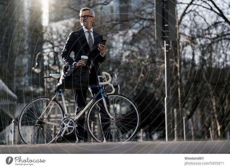 Grey-haired businessman with bicycle and coffee to go in the city Businessman Business man Businessmen Business men town cities towns bikes bicycles Coffee