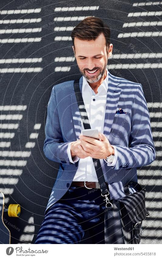 Portrait of businessman with longboard and phone near concrete wall smiling smile mobile phone mobiles mobile phones Cellphone cell phone cell phones standing