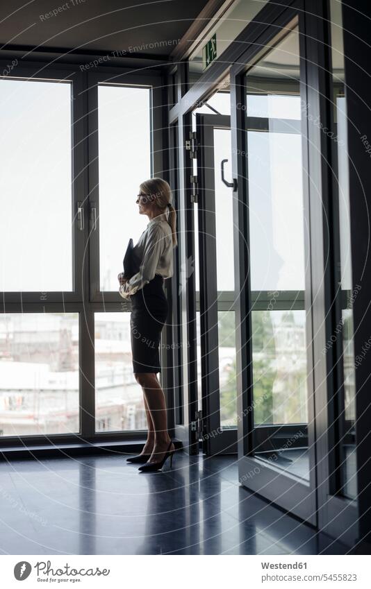 Businesswoman in office looking out of window standing businesswoman businesswomen business woman business women business people businesspeople business world