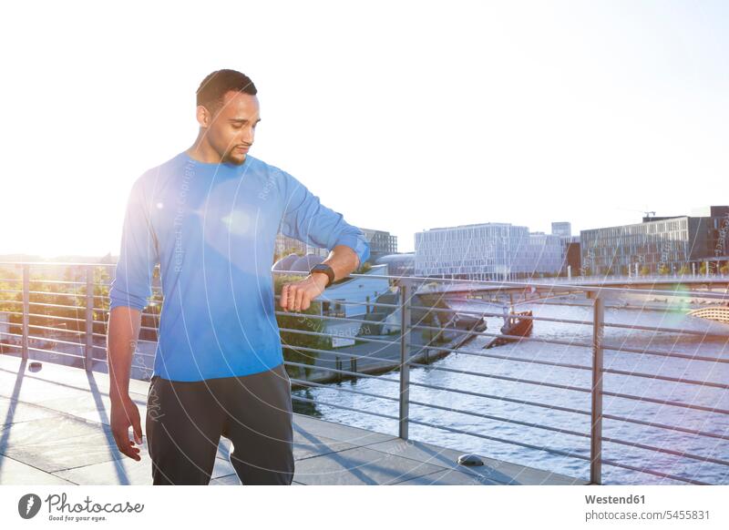 Athlete on bridge in the city checking his smartwatch serious earnest Seriousness austere fit man men males athlete Sportspeople Sportsman Sportsperson athletes