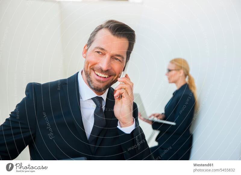Smiling businessman on cell phone and businesswoman using laptop outdoors mobile phone mobiles mobile phones Cellphone cell phones business world business life