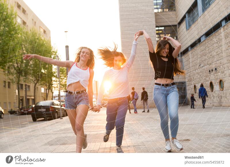 Three happy young women running hand in hand on sidewalk female friends mate friendship woman females Adults grown-ups grownups adult people persons human being