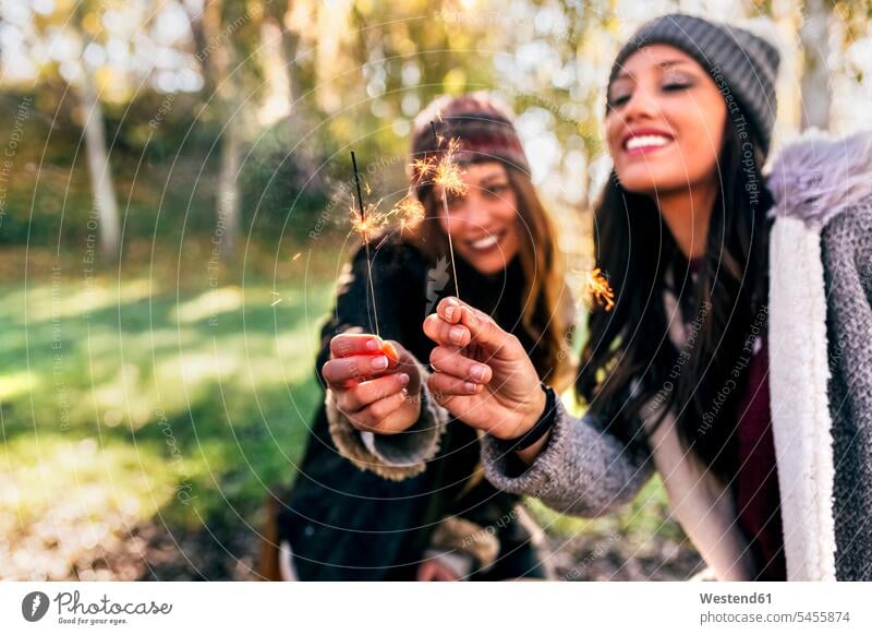 Two happy women holding sparklers in an autumnal forest woods forests fall happiness beautiful woman females female friends Adults grown-ups grownups adult