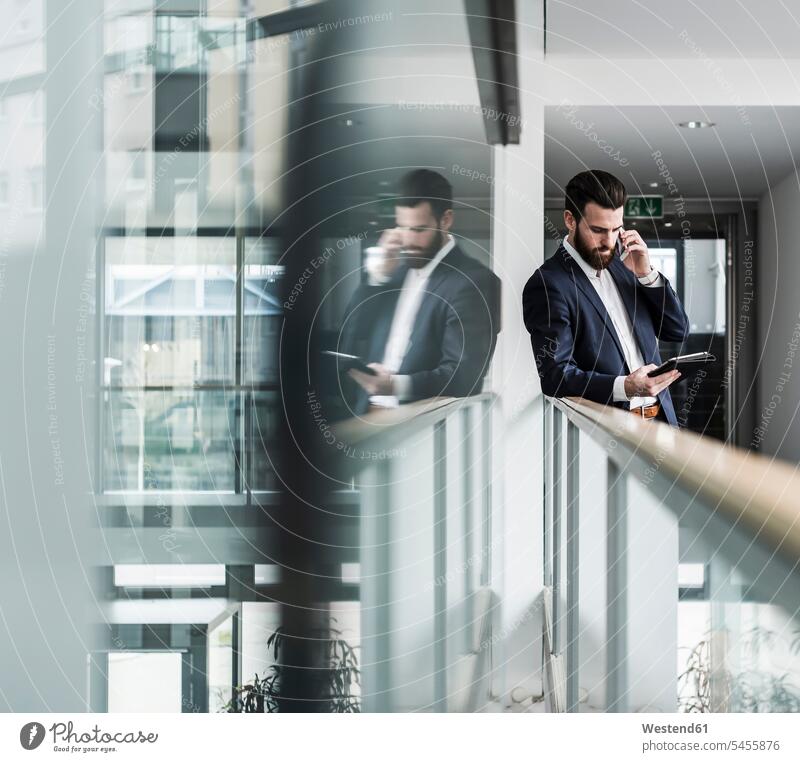 Businessman standing in office building, using smart phone and digital tablet Railing Railings accessibility accessible parapet balustrade on the move