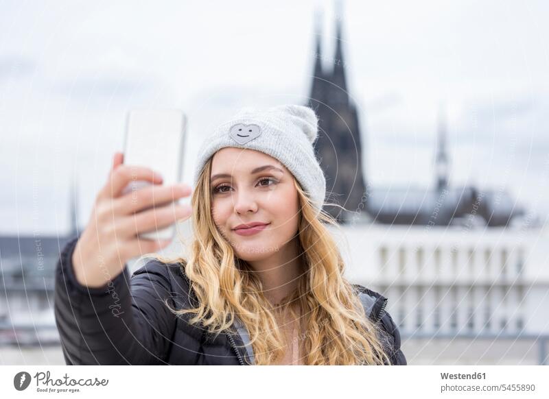 Germany, Cologne, portrait of smiling young woman taking selfie with smartphone portraits Selfie Selfies females women smile Smartphone iPhone Smartphones