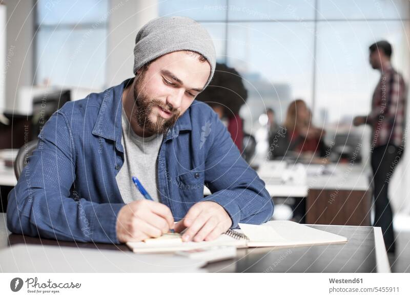 Man writing down notes at desk in office man men males noting offices office room office rooms Adults grown-ups grownups adult people persons human being humans