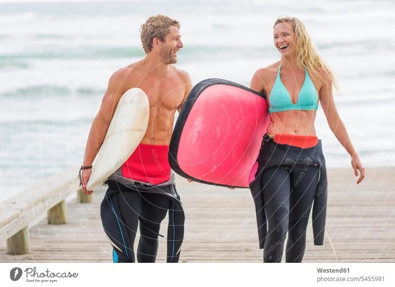 Couple walking from beach with surfboards beaches surfing surf ride surf riding Surfboarding couple twosomes partnership couples laughing Laughter going