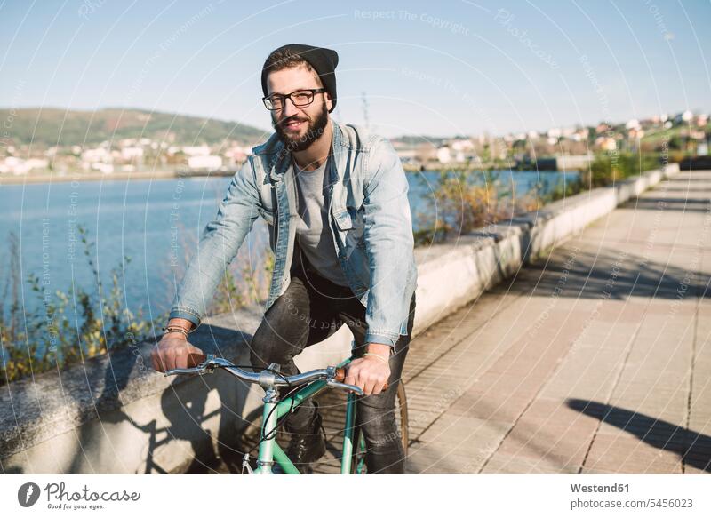Smiling young man riding his fixie bike at the waterfront men males smiling smile driving drive bicycle bikes bicycles Adults grown-ups grownups adult people