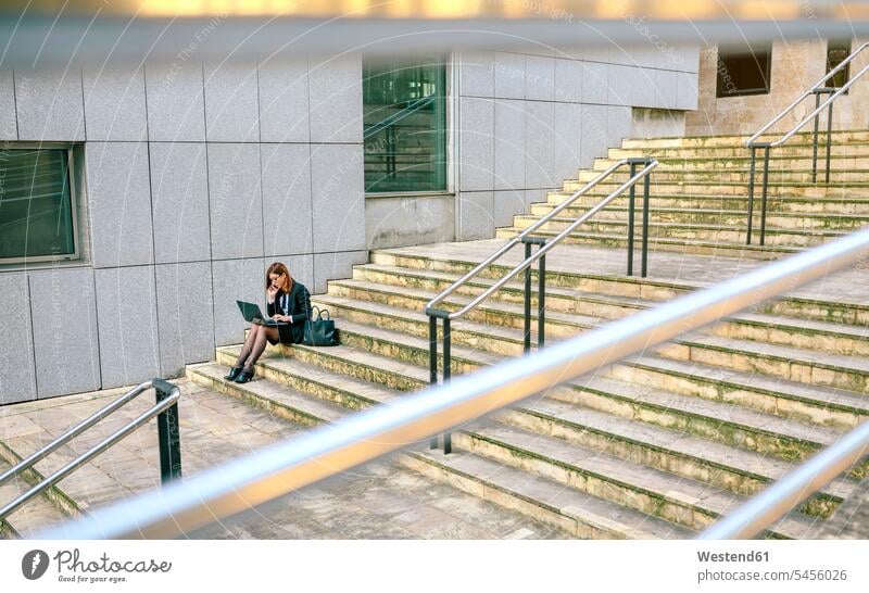 Businesswoman sitting on stairs, using laptop Seated working At Work businesswoman businesswomen business woman business women stairway using a laptop