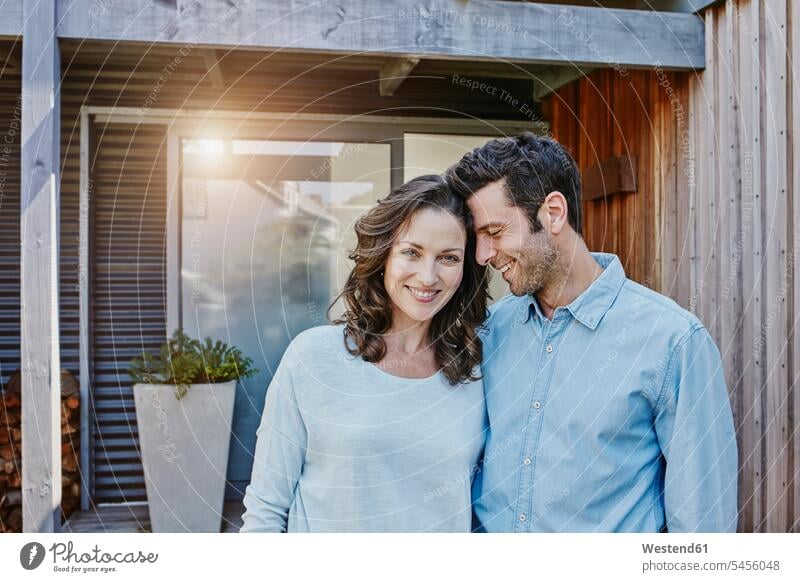 Couple standing in front of door of their home arm around arms around entrance entry Entryway entrances home ownership private owned home together couple