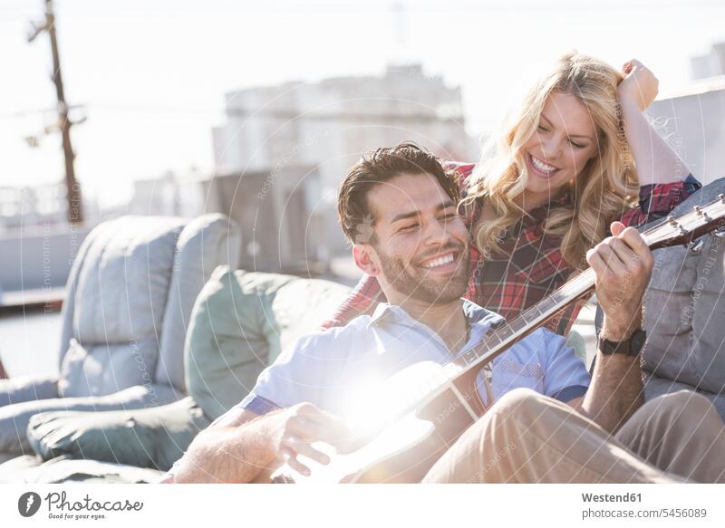 Couple on rooptop sitting on sofa and playing guitar singing musician musicians cheerful gaiety Joyous glad Cheerfulness exhilaration merry gay Seated guitars