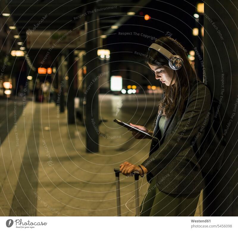 Young woman with headphones and tablet waiting at the station by night at night nite night photography females women Adults grown-ups grownups adult people