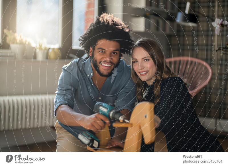 Smiling couple looking at camera mounting rocking horse with cordless drill home at home twosomes partnership couples smiling smile rocking horses people