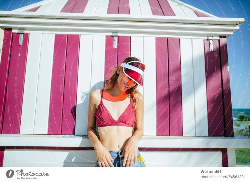 Happy young woman with bikini and sun visor in front of kiosk smiling smile females women Adults grown-ups grownups adult people persons human being humans