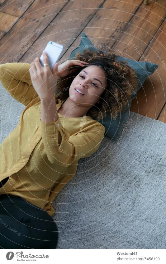 Smiling young woman lying on the floor at home with cell phone smiling smile laying down lie lying down floors mobile phone mobiles mobile phones Cellphone