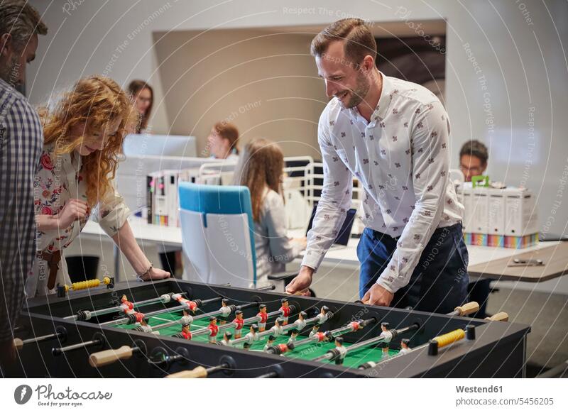 Business people in office taking a break, playing foosball table football table soccer Taking a Break resting offices office room office rooms business people