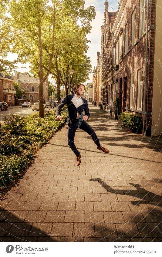 Netherlands, Venlo, happy businessman jumping on pavement Leaping Businessman Business man Businessmen Business men city town cities towns Side Walk jumps
