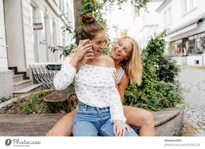 Two happy young women with cell phone in the city mobile phone mobiles mobile phones Cellphone cell phones happiness town cities towns woman females