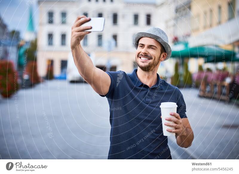Man taking selfie in the city with coffee and fedora hat - a