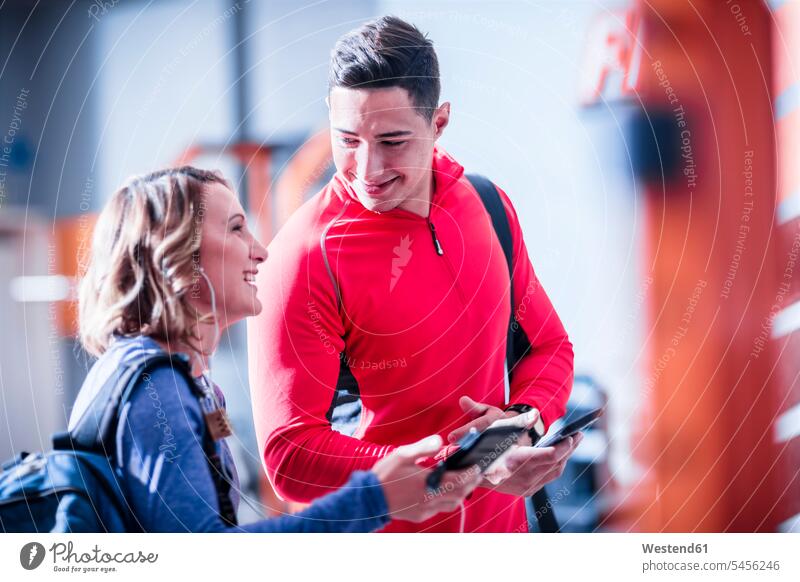 Young man and woman with cell phones and earbuds in gym smiling smile break exercising exercise training practising gyms Health Club fitness sport sports